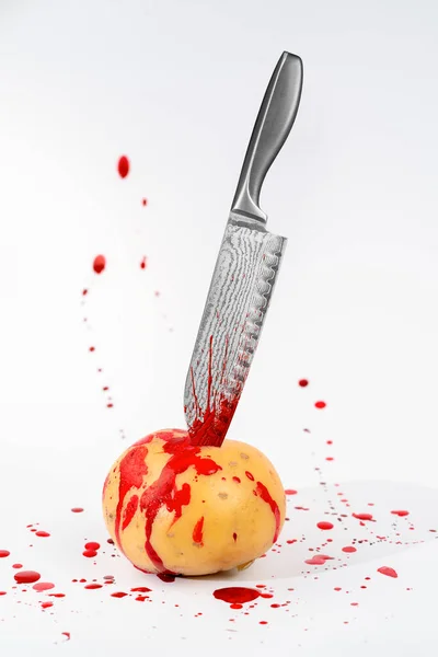 一个奇怪的主题是 一个生土豆在血淋淋的灯光下被一把有花纹的焊接厨房刀刺伤 — 图库照片