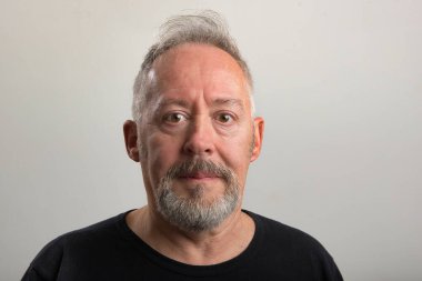 Gri arka planda sakallı ve gri saçlı orta yaşlı bir adamın yakın plan fotoğrafı.