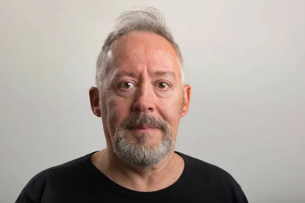 Gri arka planda sakallı ve gri saçlı orta yaşlı bir adamın yakın plan fotoğrafı.