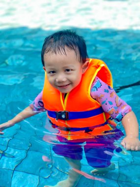 Little boy is wearing life jacket in swimming pool