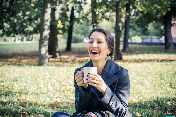 Girl in an autumn part with a white cup of hot drink — Stock Photo, Image