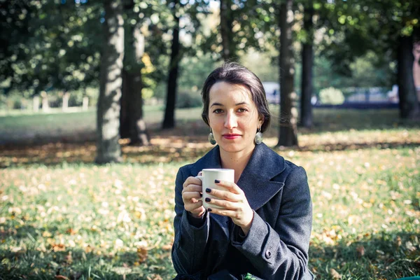 Girl in an autumn part with a white cup of hot drink — Stock Photo, Image
