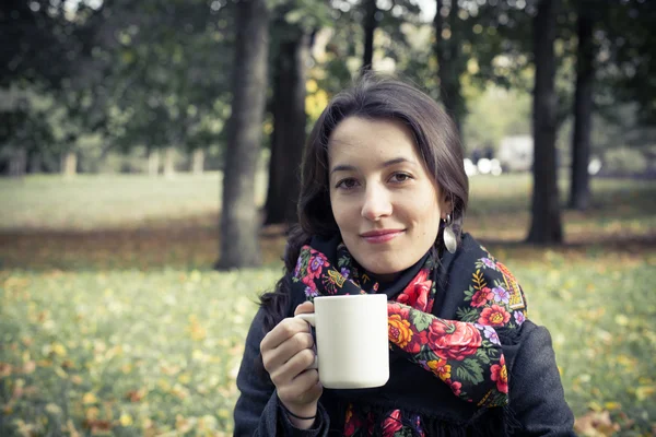 Girl in an autumn part with a white cup of hot drink — Stock Photo, Image
