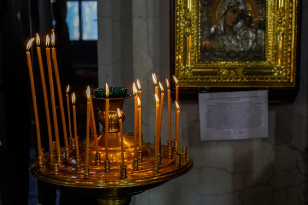 Interior de la iglesia ortodoxa rusa. Velas bajo el icono antiguo enmarcado con el oro . — Foto de Stock