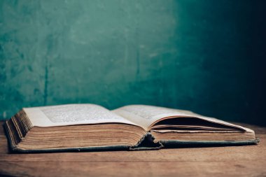 Açık antika bir kitap. Tasarım için model arka planı. Yuvarlak meşe ağacından bir masa ve yeşil duvar arkaplanı..