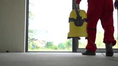 Tanınmayan tulum işçisi, elektrikli süpürgeyle beton zemini süpürüyor.