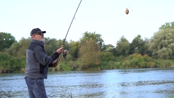 Starší muž vrhá rybářský prut, když stojí na břehu řeky. Rybaření s točící se tyčí — Stock video