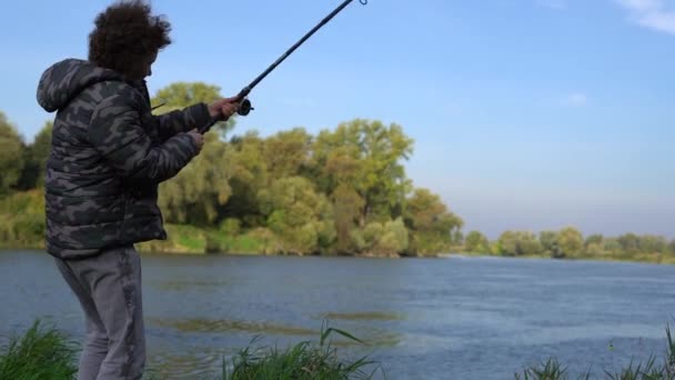 Adolescent garçon aux cheveux bouclés pêche avec une canne à filer sur le lac à l'extérieur de la ville. Passe-temps masculin concept de pêche — Video