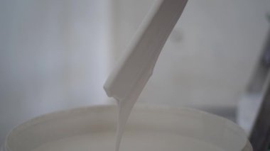 Mans elleri bir galon beyaz boyayı ahşap boya ile karıştırıyor yerde oturan karıştırıcı çubuk, yakın görüş. Yeni proje, duvarları boyamak. Erkek ressam tadilat yapıyor, evdeki işleri bitiriyor.