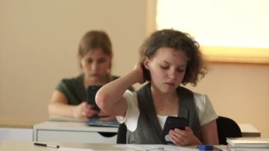 Kıvırcık saçlı liseli kız ders sırasında masasında otururken selfie çekiyor. Gözlüklü genç kız ve akıllı telefon.
