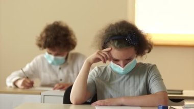 Ders sırasında koruyucu maskeli kıvırcık saçlı liseli kız. Kız maskesini çıkarıyor.