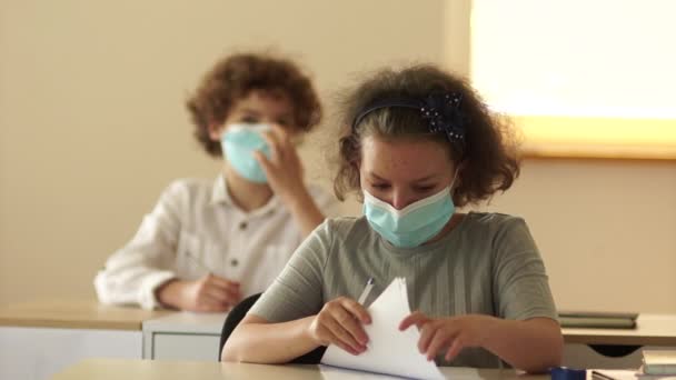 Maskerede skolebørn sidder ved deres skriveborde i klassen under den covid-19 pandemi. Børn bærer masker i klasseværelset i løbet af lektionerne – Stock-video