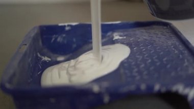 Mavi bir plastik palete dökülen beyaz yağlı boya püskürtüsünün yakın çekimi. Kalın beyaz boya, yenileme ve emlak konsepti, bitirme işi