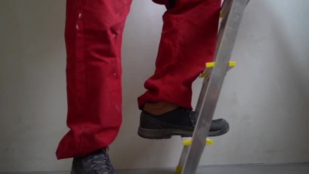 Kırmızı tulumlu, merdivene tırmanan tanınmayan bir işçinin bacakları. Yenileme, emlak ve iş bitirme konsepti — Stok video