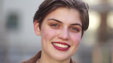 Kısa saçlı ve kırmızı rujlu güzel bir kızın yakın portresi. Beyaz dişli gülümseme. Kadın çerçeveye bakar ve yüzünü çevirir.