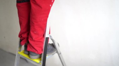Olgun erkek işçi merdiven üzerinde dururken tavanı beyaz boyayla boyar. Yenileme ve iç kaplama kavramı