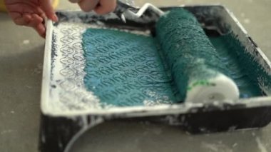 Yenileme ve iç kaplama konsepti. İşçi, beyaz boyayı plastik inşaat paletinde rulo ile karıştırıyor ve duvarları boyamaya hazırlanıyor. DIY onarımı. Ev atölyesi
