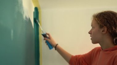 Genç kıvırcık saçlı genç kızın yakın portresi duvarı patenli bir griye boyuyor. Evdeki oda tadilatı. Yaratıcılık ve yenileme konsepti