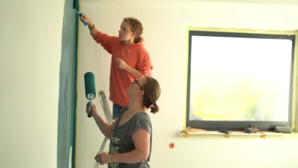 十多岁的女儿，带着母亲的彩绘墙壁，涂上了绿色的苦艾酱。快乐的家庭在他们的新家做装修。母亲节。革新和创造概念 — 图库视频影像