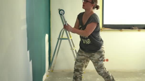 用滚筒把年轻女子漆成深蓝色的墙关上。女设计师在墙上涂漆.维修工作的概念和改善住房条件 — 图库视频影像