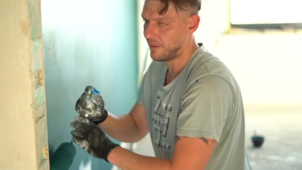 一个涂漆滚筒的男性房屋漆工的肖像。更新期间，手里拿着滚筒的年轻人在油漆墙壁，看着相机笑了 — 图库视频影像