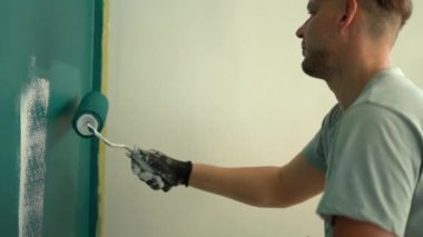 Boyacı ve boyacı bir adamın portresi. Duvarı maviye boyayan genç adam, yenileme ve emlak konsepti