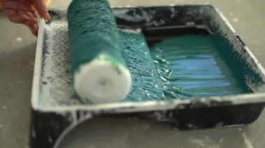 Bir işçinin yakın plan çekimi bir silindiri mavi boya tepsisine daldırır. Hızlandırılmış oynatma. Duvarları yenileme ve boyama konsepti