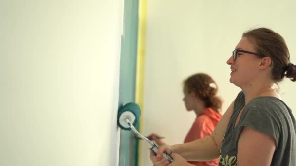 Ibu dan anak perempuan dewasa melukis dinding dengan rol di rumah mereka. Lakukan sendiri. Turquoise atau warna adriatic, renovasi interior di rumah — Stok Video