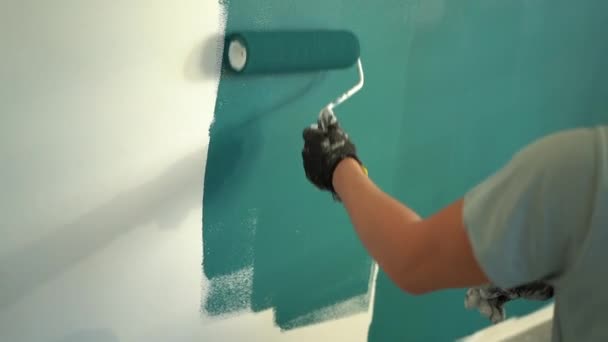 Młody wysoki mężczyzna maluje ścianę na zielono dużym wałkiem malarskim. Remont domu i nowe nieruchomości. Koncepcja kredytu hipotecznego — Wideo stockowe