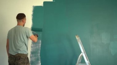 Arkadan bak. Genç uzun boylu erkek, büyük bir boya silindiri kullanarak bir duvarı yeşile boyar. Ev tadilatı ve yeni gayrimenkul. İpotek kavramı