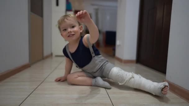 Gelukkig schattig peuter, na een toevallige breuk van zijn been, beweegt rond het appartement met een gips gegoten. Thuis een gebroken been terughalen, ziektekostenverzekering — Stockvideo