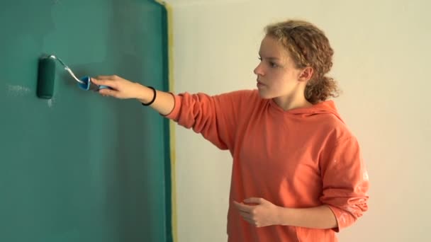 Teen girl makes a renovation in her own room. Renovation and creativity. Beautiful young girl paints the wall blue while standing on a stepladder — Stock Video