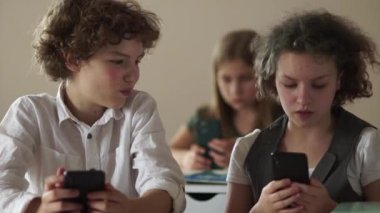 Kıvırcık saçlı gençler okulda ders sırasında akıllı telefonlarına bakarlar. Ergenler arasında takıntı, okula dönüş.