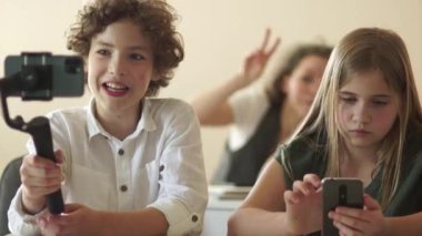 Kıvırcık saçlı bir gencin portresi. Elinde bir bukle var. Bir okul çocuğu bir okul sınıfından bir dereyi kaydediyor. Video günlüğü ve hikaye kavramı