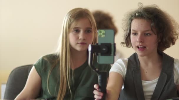 Twee meisjes nemen een video op school op. Een meisje met een strookje en een smartphone in haar handen. Elektronische stabilisator en video blog concept — Stockvideo