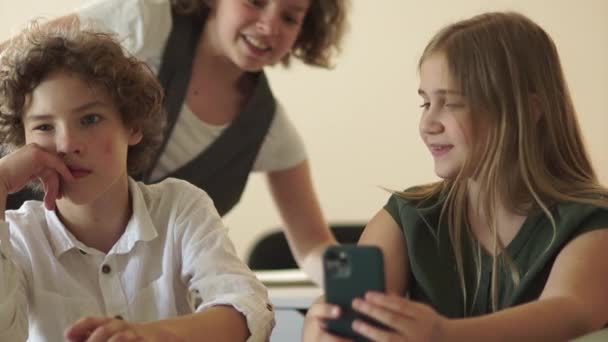 Mädchen macht ein Selfie. Teenager werden fotografiert, ein Junge und zwei Mädchen an einem Schreibtisch mit Smartphone — Stockvideo