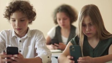 Çevrimiçi oyunlar ve çocuklar. Sınıf arkadaşları, bir erkek ve bir kız, okul masasında oturuyorlar ve akıllı telefonlarının ekranlarına bakıyorlar. Okula dönün, çocuklar ve aletler.