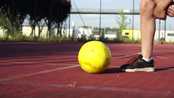 Primer plano de una pelota de fútbol amarillo en un campo de deportes abierto junto a un pie de hombre en una zapatilla de deporte. Concepto de vida deportiva, actividad de estilo de vida — Vídeos de Stock
