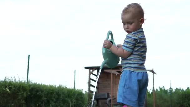 Härligt blont barn vattna sängarna med en grön plast vattenkanna. Liten trädgårdsmästare, lycklig barndom — Stockvideo