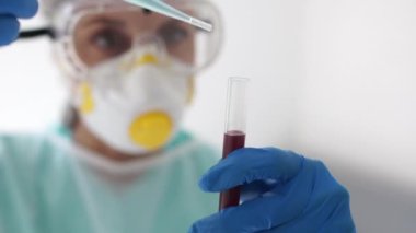 Koruyucu kıyafetli ve elinde deney tüpü olan bir maske takmış erkek bir mikrobiyolog portresi. Kan plazma örneği, Covid-19 koronovirüs testi.