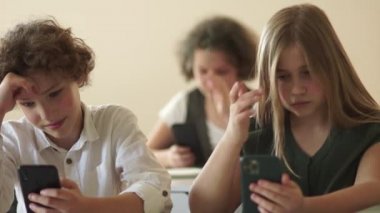 Bir erkek ve bir kız akıllı telefonlarını kullanarak online oyun oynuyorlar. Okuldaki çocuklar masalarında otururken akıllı telefon kullanıyorlar.