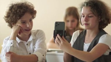 Komik blogcu kız akıllı telefonu için dengeleyiciyi ayarlamaya çalışıyor ve hata yapıyor. Çocuklar akıllı telefon, okul çocukları ve sosyal ağlarda video kaydederken gülüyorlar