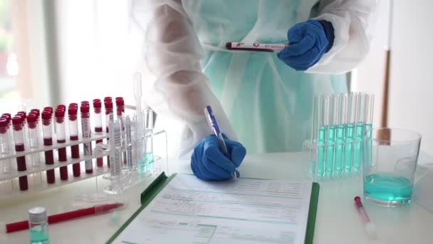 Closeup of microbiologist or medical worker hand with blue surgical gloves marking blood test result as positive for the new rapidly spreading Coronavirus. Laboratory research of a new strain omicron — Stockvideo