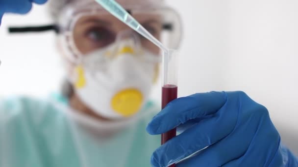 Close-up portret van een vrouwelijke microbioloog arts in een beschermend pak en een masker met een reageerbuis in zijn handen. Bloedplasma monster, Covid-19 coronovirus test — Stockvideo
