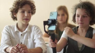 Kız ve erkek, okuldaki bir blog için video çekiyor. Dengeleyicisi olan bir okul blogcusunun portresi. Sınıfta cep telefonuyla ders çalışan ve blog yazan sevimli sınıf arkadaşları.