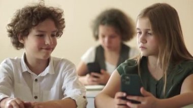 Güzel, uzun saçlı genç kız okulda masasında otururken sınıf arkadaşıyla selfie çekiyor. Çocuklar ve aletler konsepti