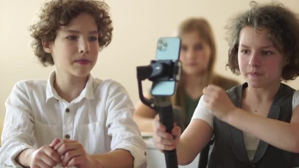 Garçon et fille filmant une vidéo pour un blog à l'école. Portrait d'une écolière blogueuse avec un stabilisateur. Adorables camarades de classe drôles étudier et bloguer via téléphone portable en classe — Video