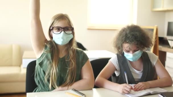 Η μαθήτρια που φοράει μάσκα σηκώνει το χέρι της, έτοιμη να απαντήσει. Παιδιά στην τάξη μετά από καραντίνα coronavirus covid-19, πίσω στο σχολείο, μετά την καραντίνα ζωή, νέα κανονικότητα — Αρχείο Βίντεο