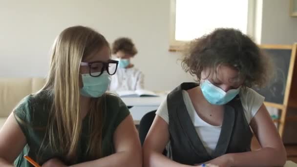 Lesson in the classroom in high school. Masked children in the classroom, write a test paper. Post-quarantine life, back to school. Schoolgirls wearing masks write in their notebooks — Vídeo de Stock