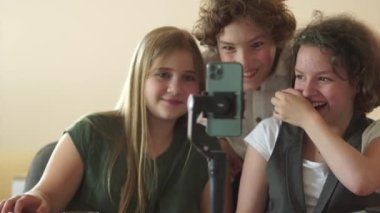 Üç okul çocuğu bir sınıfta akıllı telefonun önünde bir video çekiyorlar. Komik çocuklar eğlenir ve güler.